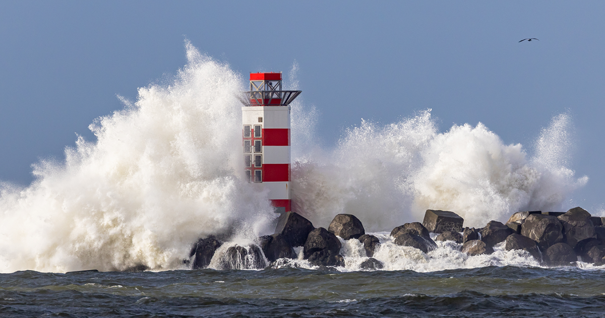 Door de harde wind ontstaan er hoge golven tegen een vuurtoren aan