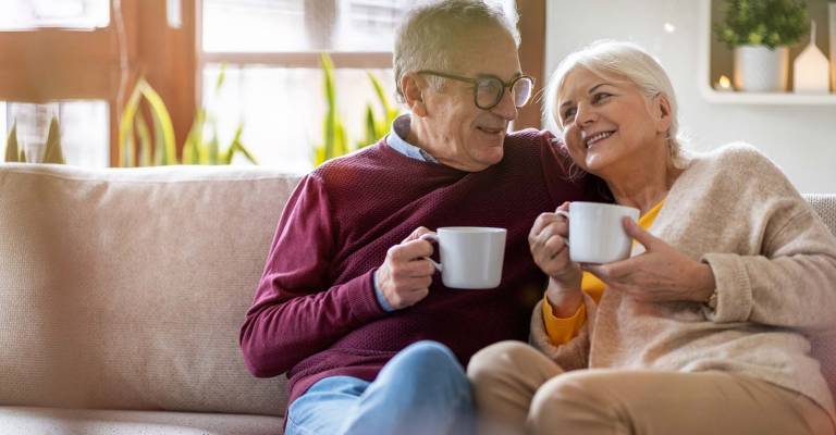 Gelukkig senior paar thuis op de bank met een kop koffie