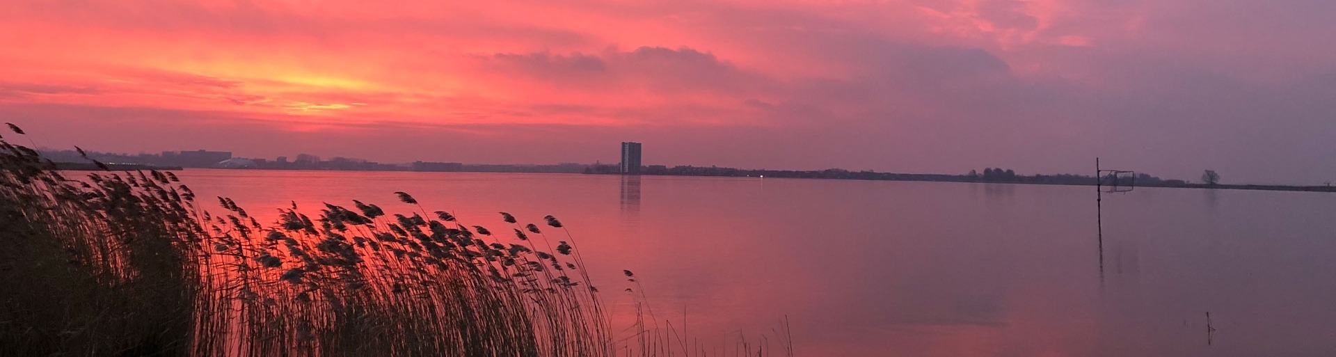 Een ondergaande zon met uitzicht over water en op de achtergrond flatgebouwen